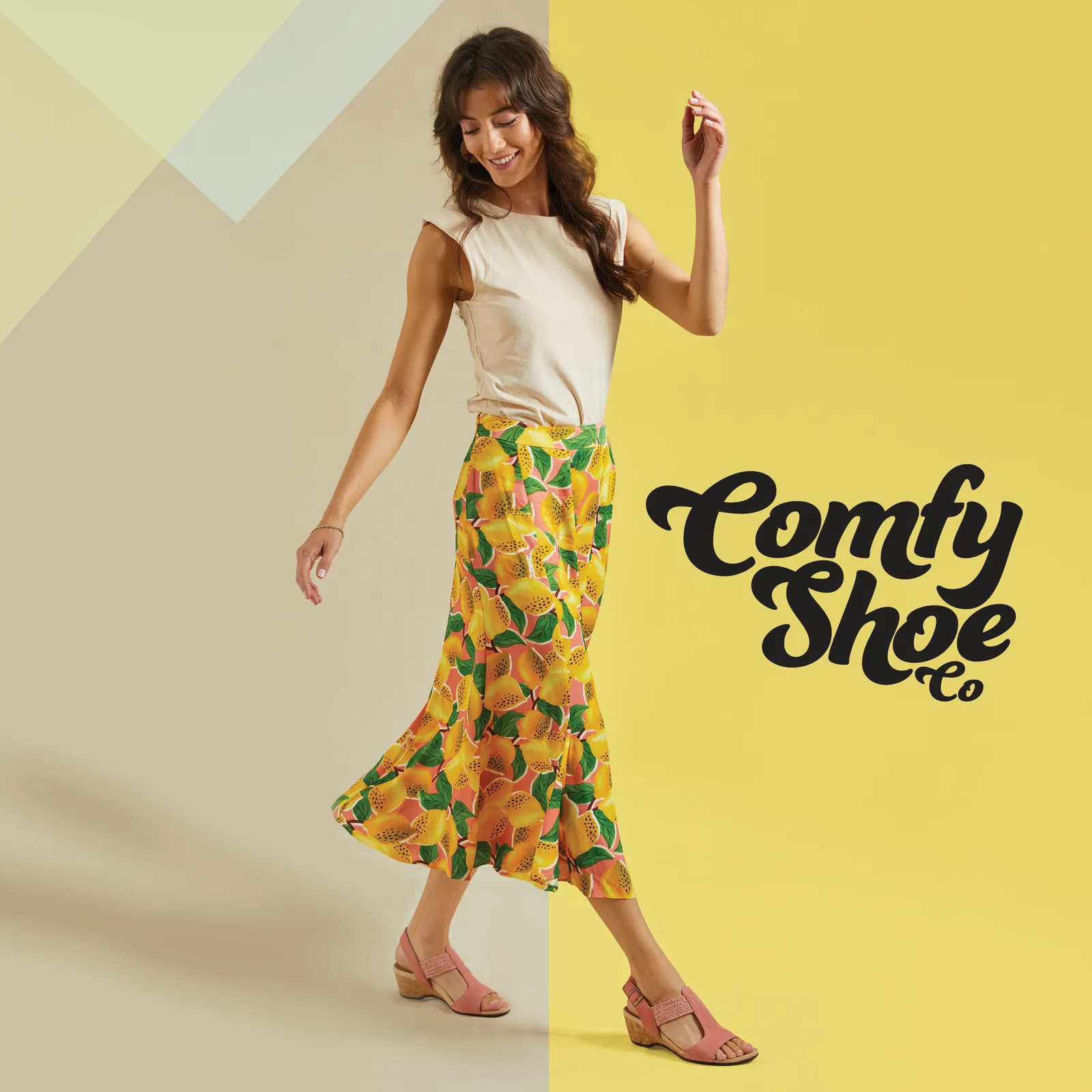 Comfy Shoe Co model wearing a fruit print skirt and pink wedge sandals against a yellow background