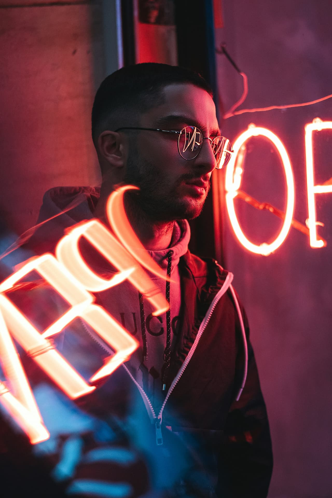 Man in glasses lit by a red neon OPEN sign at night