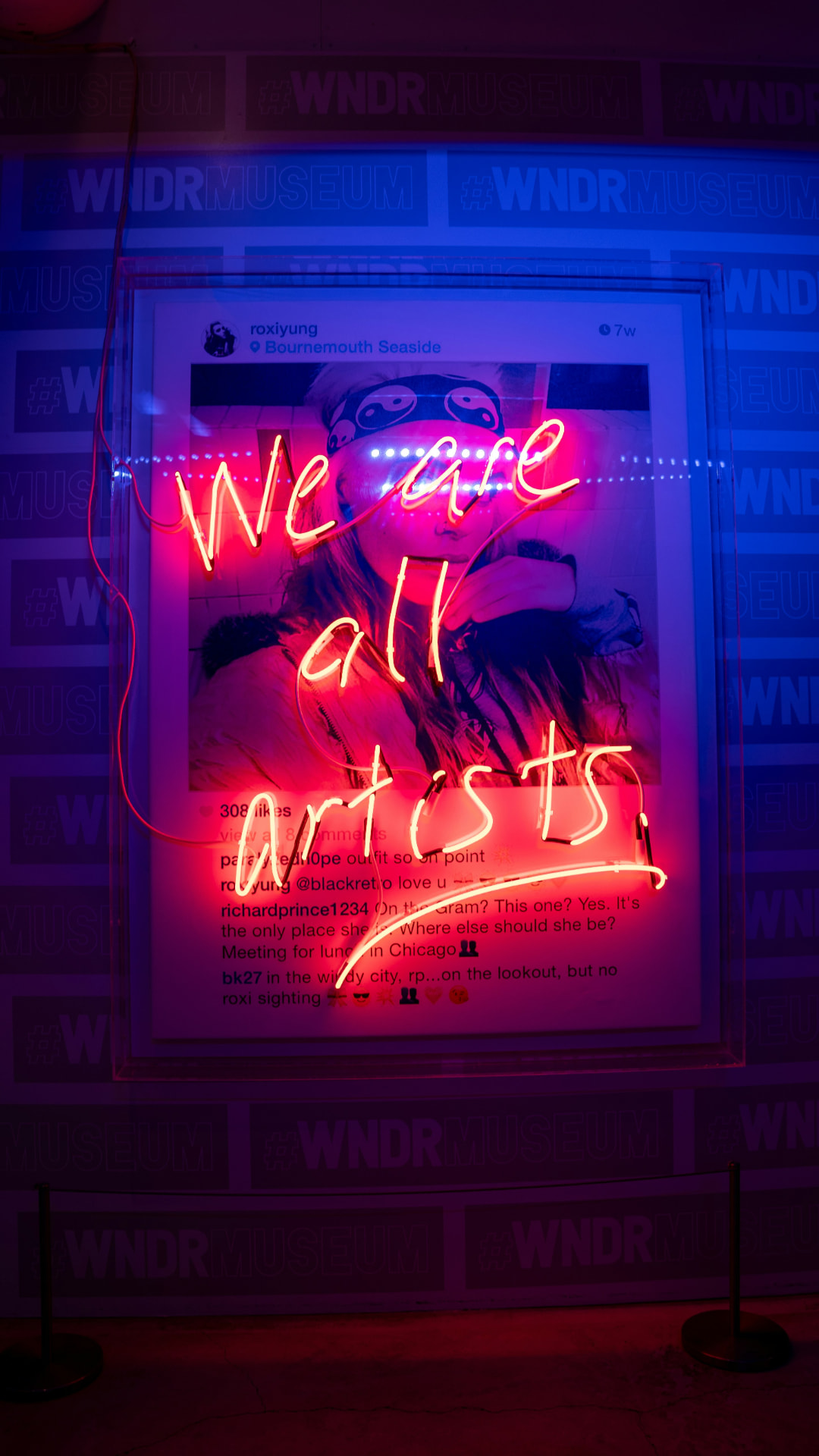 Neon sign reading We are all artists glowing over a framed print