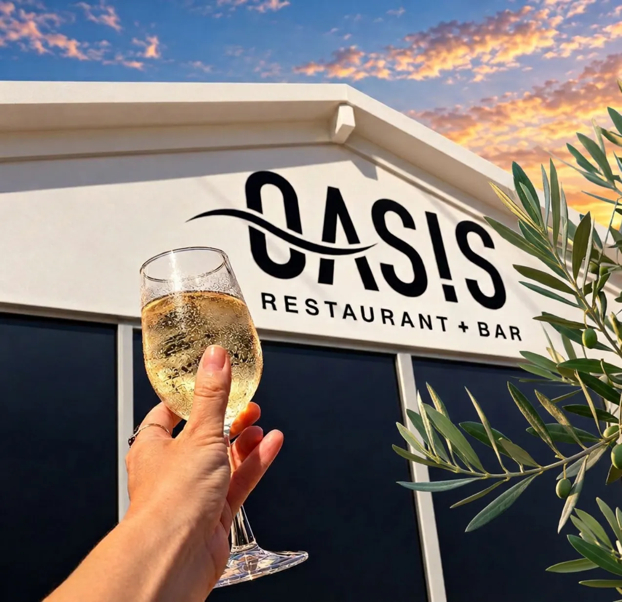 Hand raising a glass of wine in front of the Oasis Restaurant and Bar sign at sunset with an olive branch