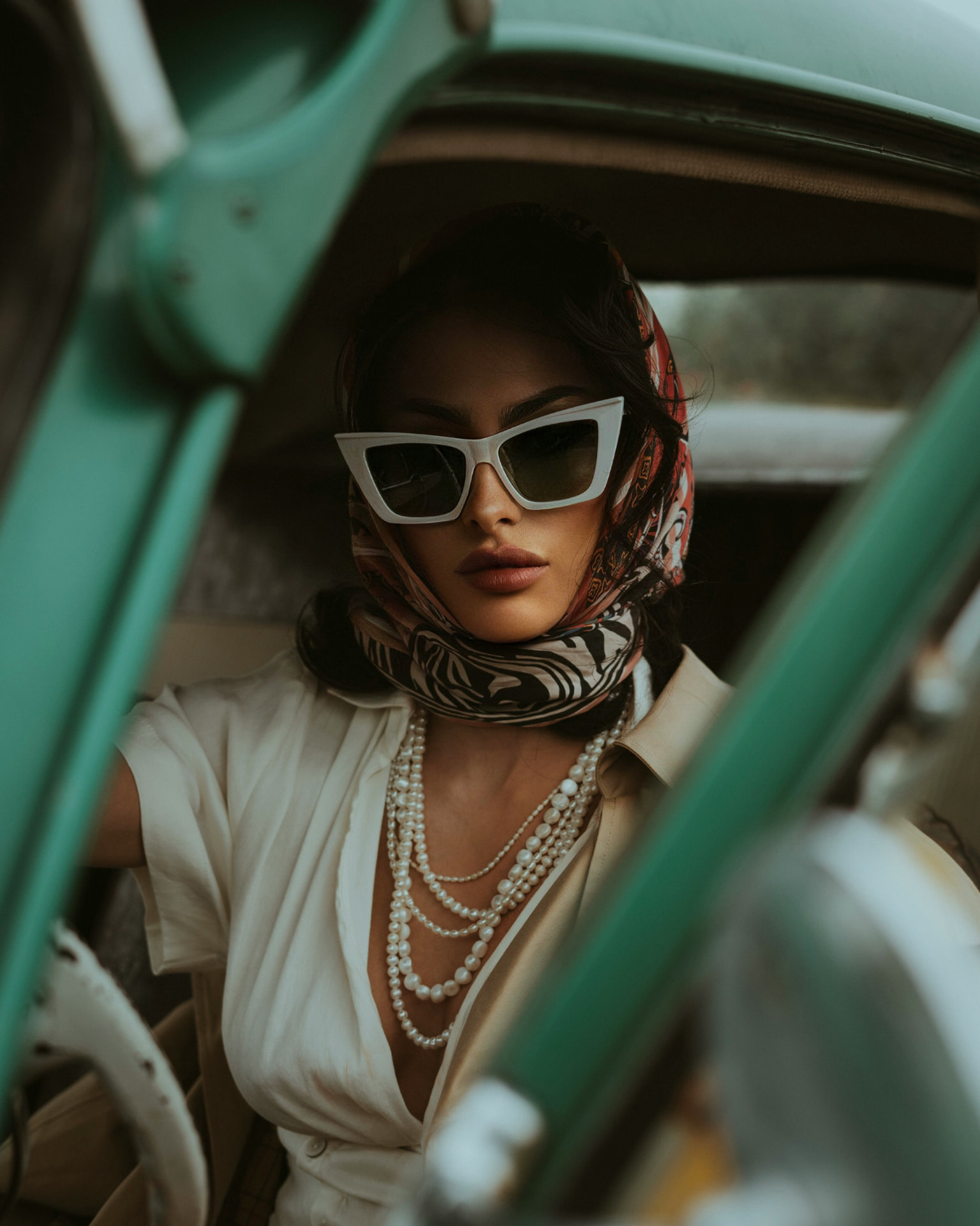 Portrait of a woman in sunglasses and headscarf beside a vintage car